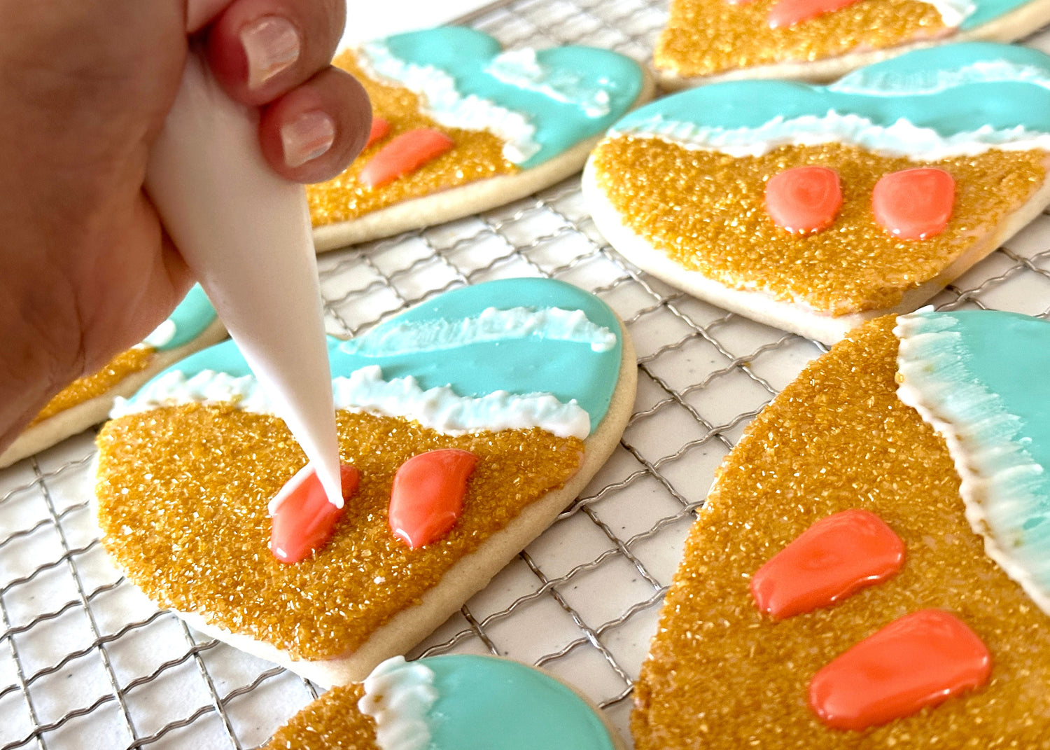 Decorating heart-shaped cookies with gold icing, blue and pink accents on a cooling rack.